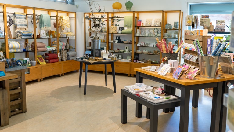 A light room with elegant shop displays on tables, stools and shelves.